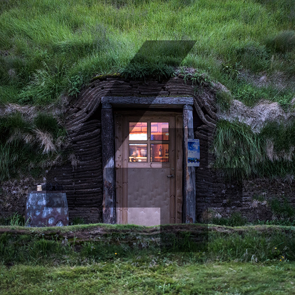 A Hobbit style house built into the side of a hill with a tan door and an interior light on